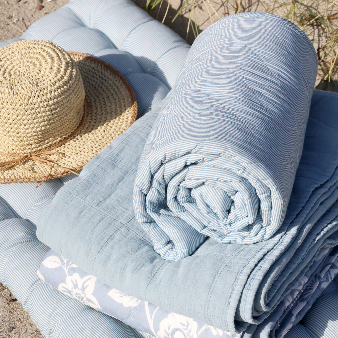 Zusammengerollter Chic Antique Vintage Quilt Sky Blue auf gepolsterter Sitzauflage am Strand