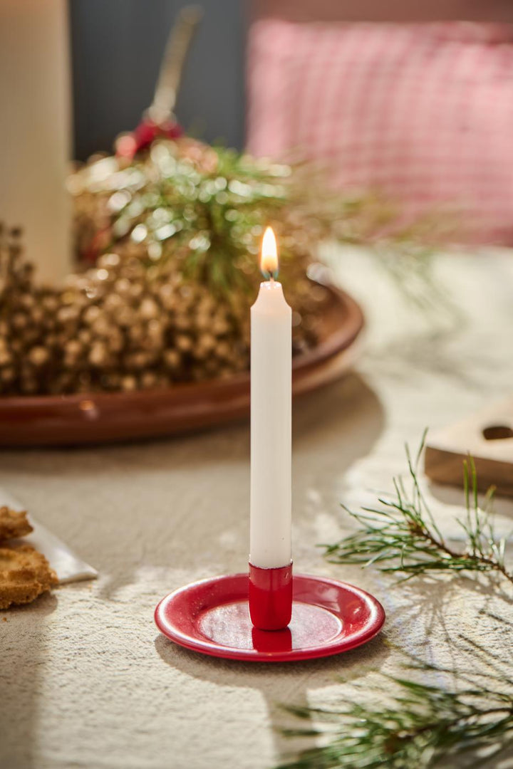 Weiße Stabkerze von Ib Laursen in rotem Kerzenhalter auf weihnachtlich dekoriertem Tisch mit Tannenzweig und Gebäck