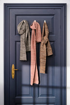 Ib Laursen gestrickte Halstücher mit Melange-Struktur in Grau, Rosa und Braun an Haken vor blauer Tür im skandinavischen Stil