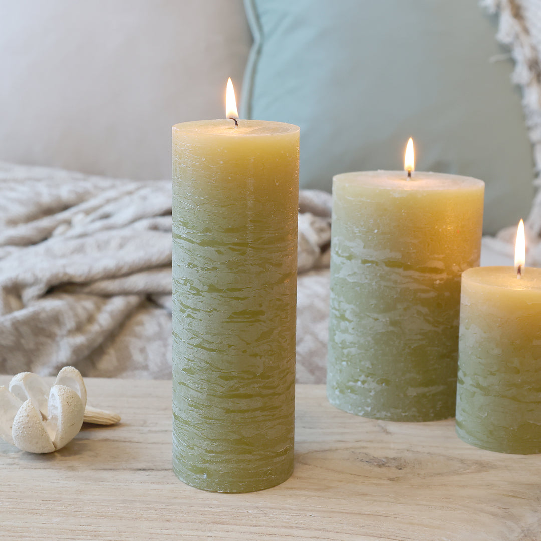 Chic Antique Macon Stumpenkerze in Moos, 20 cm hoch, brennend auf Holztisch dekoriert mit weiteren Kerzen im Hintergrund