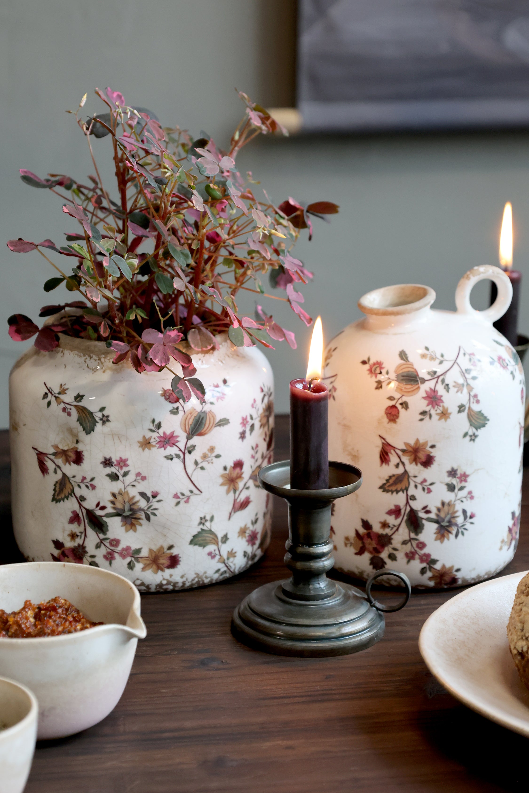Chic Antique Kammerleuchter in Antique Messing aus Eisen mit Stabkerze, dekoriert auf Holztisch neben floralen Keramikvasen im Landhausstil