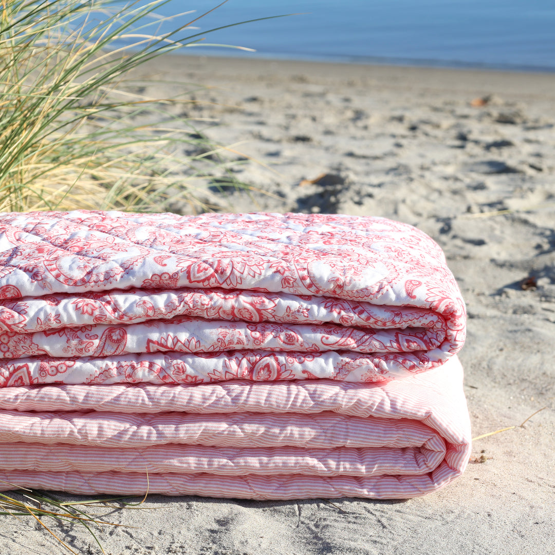 Gefalteter Chic Antique Aix Vintage Quilt mit rosa weißem Paisley Muster am Strand