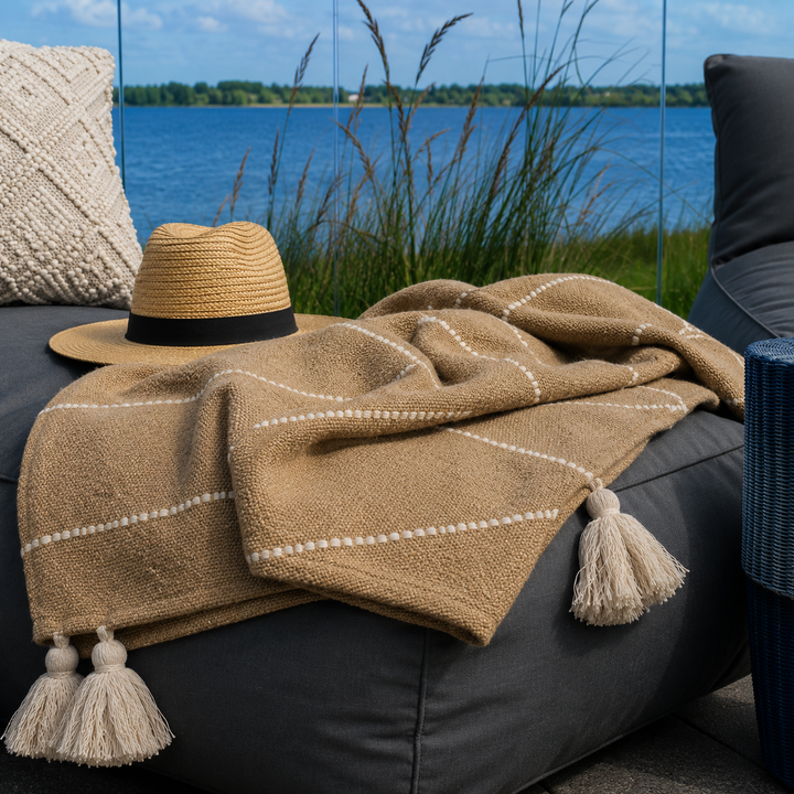 Alttext: Braunes Chic Antique Plaid mit Quasten auf gemütlicher Terrasse am Wasser im Landhausstil