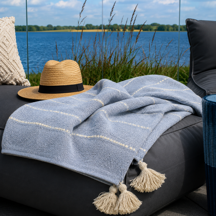 Alttext: Hellblaues Chic Antique Plaid mit Quasten auf Outdoor Lounge am See