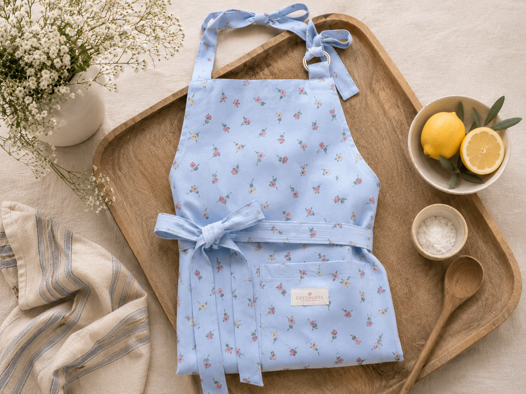 GreenGate Kinderschürze Hellblau mit floralem Muster als Flatlay auf Holztablett mit Zitronen und Küchenaccessoires im Landhausstil