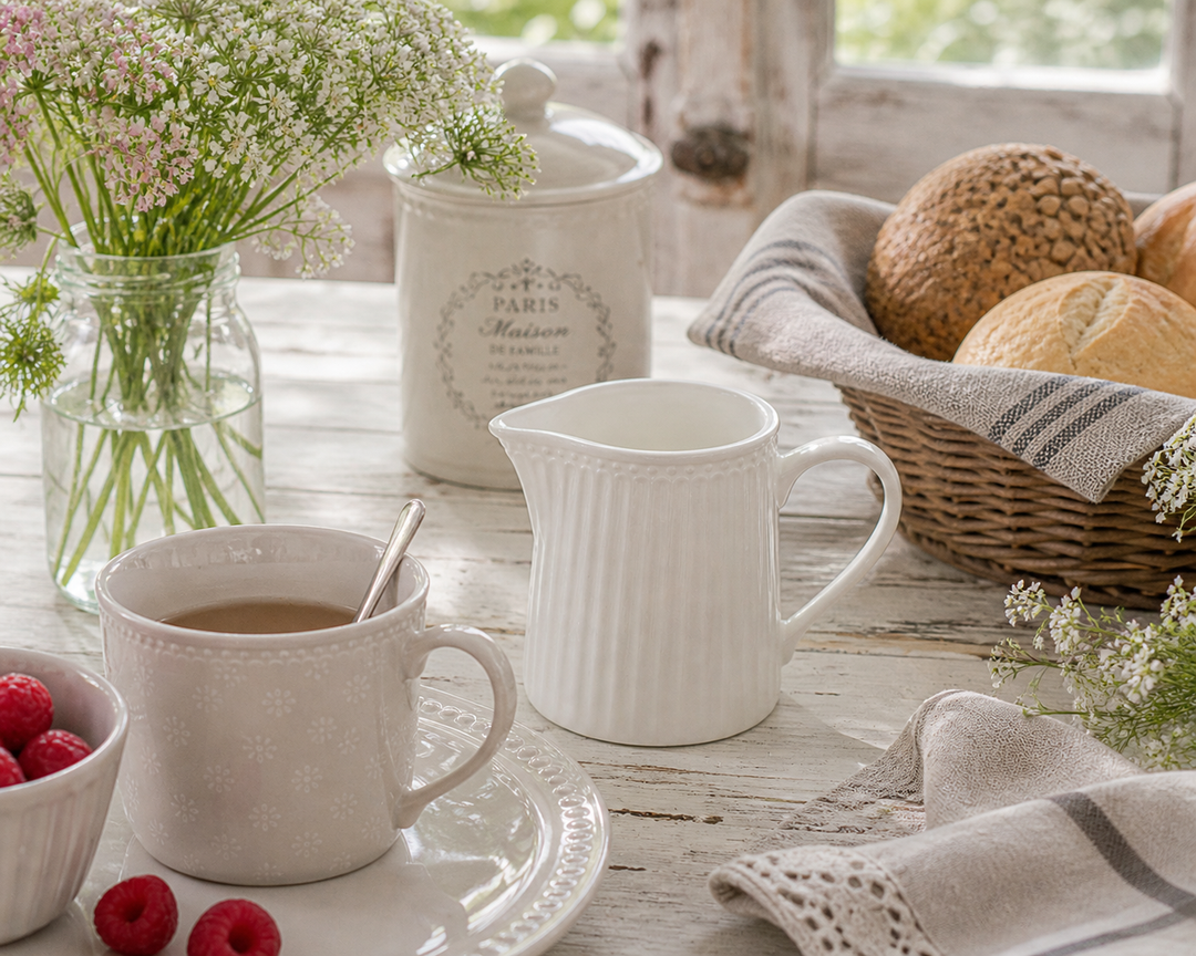 GreenGate Milchkännchen Alice Weiß auf rustikalem Landhausküchentisch mit Tasse, Blumen und Frühstück im skandinavischen Stil