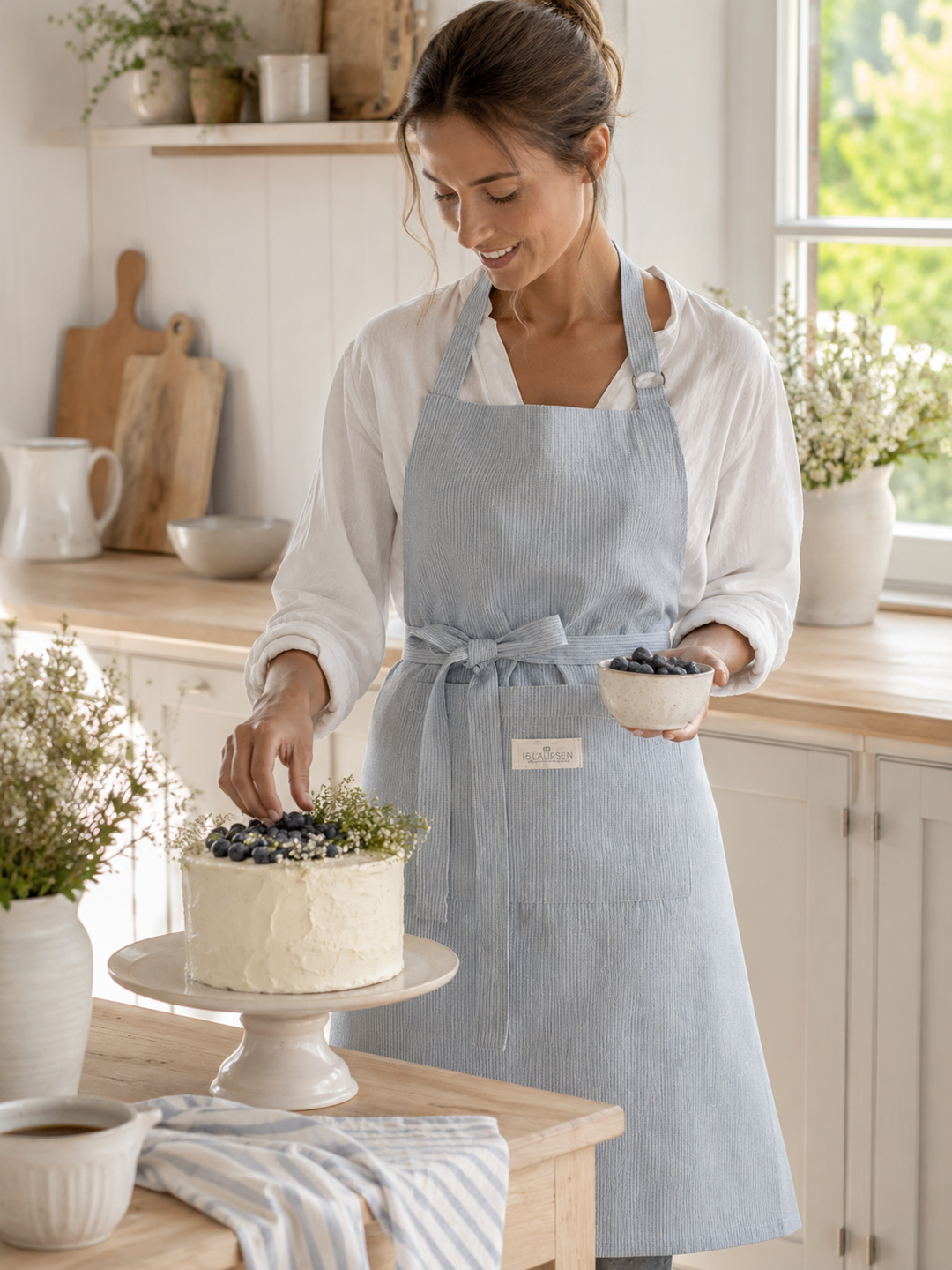 GreenGate Schürze Alice Hellblau aus Baumwolle mit feinen Streifen in heller skandinavischer Landhausküche beim Backen