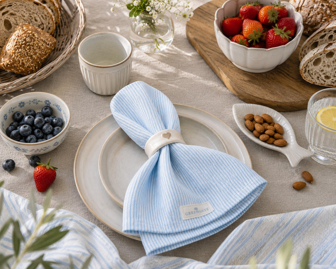 GreenGate Stoffserviette Alicia hellblau auf gedecktem Frühstückstisch mit Beeren, Brot und heller Landhausdekoration