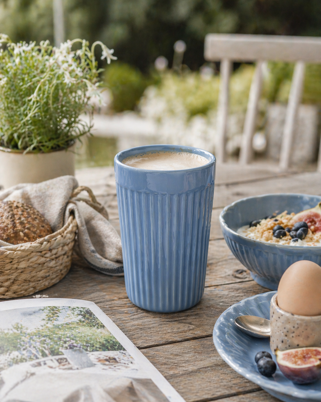 IB Laursen Mynte Café Latte Becher Blue Bell in Nutzung auf Terrasse beim Frühstück mit Kaffee, Schale und skandinavischer Outdoor Tischdekoration
