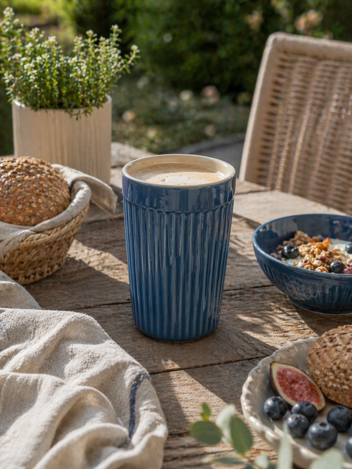 IB Laursen Mynte Café Latte Becher Cornflower in Nutzung auf Terrasse beim Frühstück mit Kaffee, Schale und skandinavischer Outdoor Tischdekoration