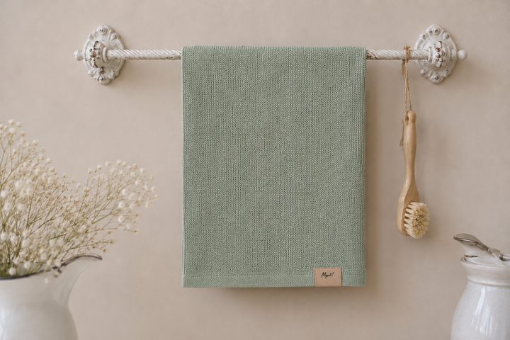 IB Laursen Mynte Geschirrtuch staubig grün an dekorativer Vintage Handtuchstange im hellen Landhausstil mit Schleierkraut und Keramikdeko